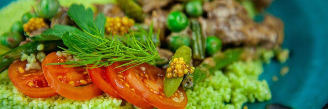 Close-up of a colorful green couscous salad with tomatoes and fresh herbs.